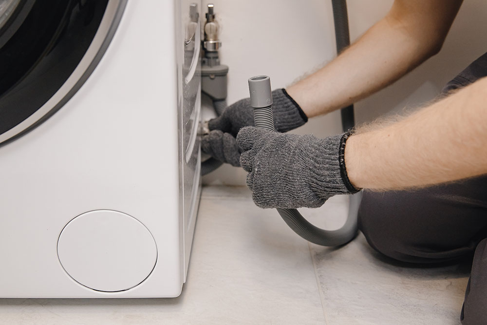 Plumber repairing washing machine, working man fixing connects pipe to drain water